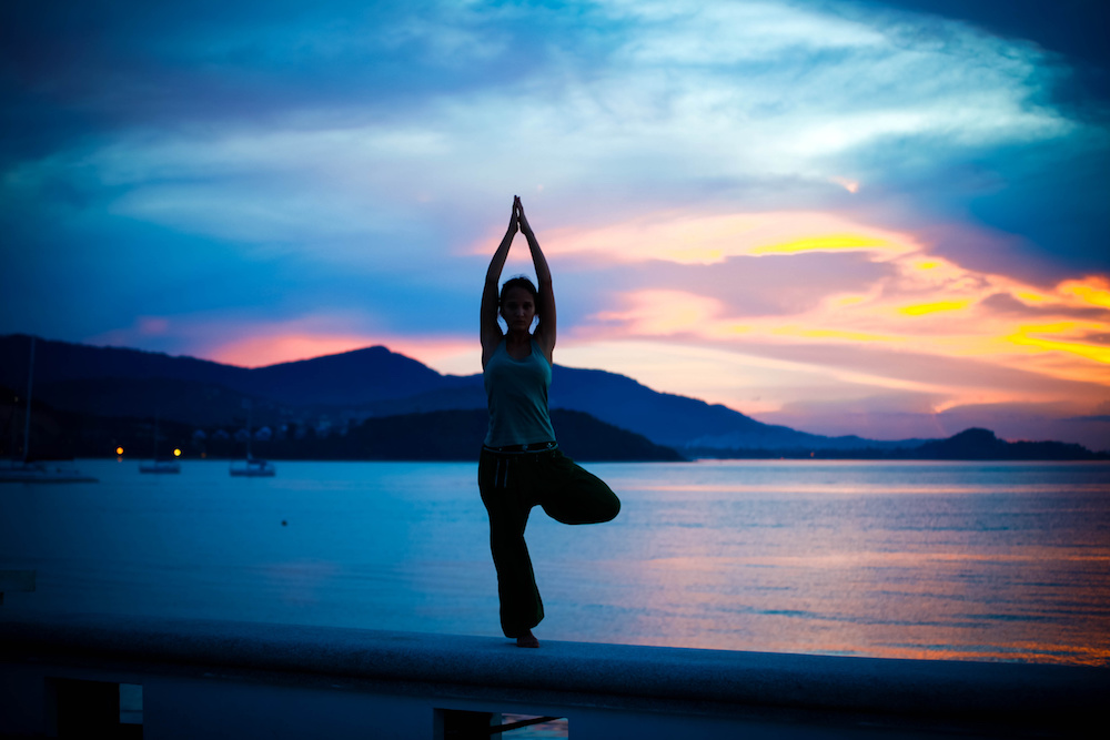 young woman doing yoga exercise on the background of amazing sunset.